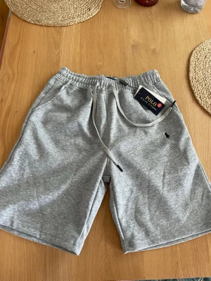 Polo Ralph Lauren shorts - Snygga grå sweatshorts från Polo Ralph Lauren med elastisk midja och snörning. Klassisk logga broderad på vänster ben. Perfekta för chill dagar eller träning, tillverkade i mjuk bomullsmix för maximal komfort. Storlek M. Riktigt sköna. Kom privat vid minsta frågor!