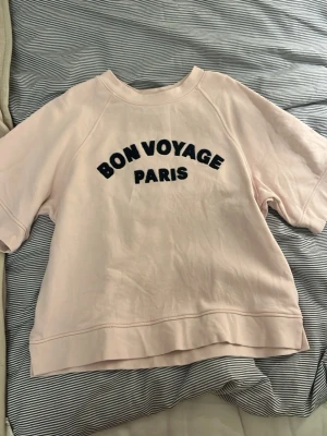 Ljusrosa sweatshirt med tryck - Helt ny endast använd 1 gång, kortärmad ljusrosa sweatshirt med texten 'BON VOYAGE PARIS' i svart på bröstet. Om ni har mer frågor och tröjan och passformen är det bara att kontakta mig 💗 