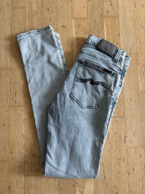  Nudie jeans  - Snygga ljusgrå jeans i slim fit-modell med klassiska fem fickor och svarta broderade detaljer på bakfickorna från märket Nudie jeans. Väldigt bra skick ej använd mycket allts. Modellen heter high kai 