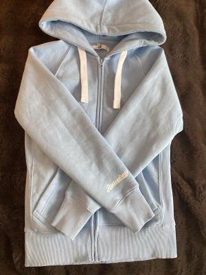 Ljusblå hoodie från Russemerch - Ljusblå hoodie med dragkedja från Russedress. Köpte för 750 kr men öppen för prisförslag! (Endast använd 1 gång)
