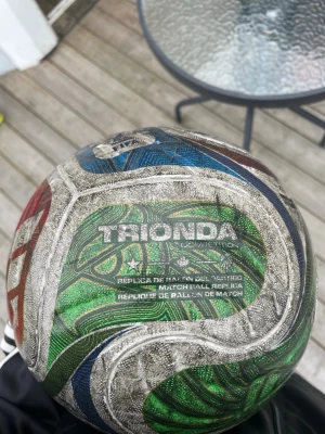 Färgglad fotboll Trionda Competition - Säljer en fotboll av modellen Trionda Competition. Bollen har ett mönster i grönt, blått, rött och silver med text och stjärndetaljer. Perfekt för matcher eller träning på planen. Snygg design som sticker ut bland andra bollar.