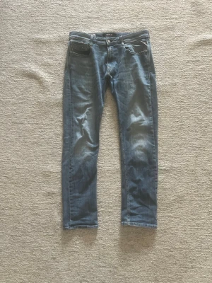 Blå jeans från Replay, modell Rocco - Snygga blå jeans från Replay i modellen Rocco. Jeansen har klassisk femficksdesign, raka ben och slitningar för en avslappnad look. Tillverkade i mjukt denimtyg som ger en skön passform. Perfekta för dig som gillar en casual stil.