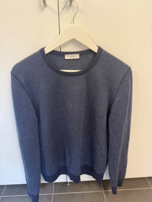 Blå stickad tröja från Gran Sasso, stl 50 M/L i 100% Virgin Wool - Snygg blå stickad tröja från Gran Sasso med rund halsringning och diskret struktur i materialet. Tröjan har långa ärmar och ribbade muddar vid ärmslut och nederkant. Perfekt för dig som gillar klassisk och stilren design. NYPRIS 2500kr