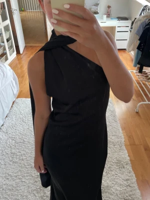 Satin balklänning - Snygg svart balklänning med en elegant drapering över axeln. Klänningen har en smal passform och ett långt fall. Fin klänning till bal, fest eller liknande!!