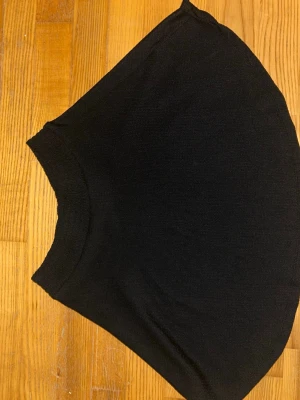 Svart tight ribbad kortkjol XS/S - En svart tight kortkjol i ribbad bomull med stretchig midja. Kjolen har en enkel och stilren design som är lätt att matcha med olika toppar och sneakers. Perfekt för dig som gillar en basic look med lite edge.