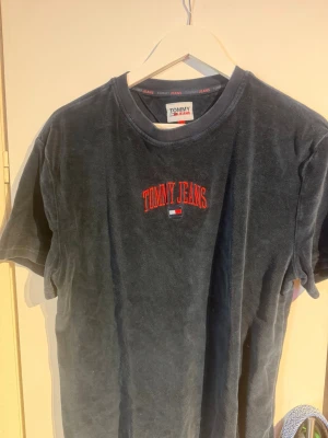 Mörkblå t-shirt från Tommy Jeans - Mörkblå t-shirt från Tommy Jeans med röd broderad logga på bröstet. Klassisk rund halsringning och korta ärmar. Tillverkad i mjuk bomull som känns skön mot huden. Perfekt för en avslappnad och stilren look.