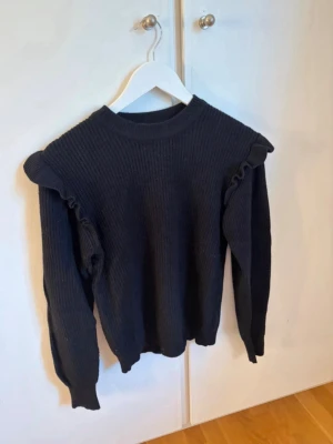 Stickad tröja - Svart stickad tröja med volang vid axlarna.