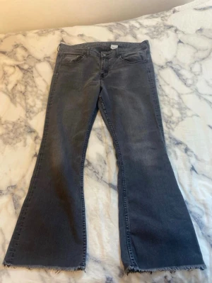 Gråa bootcut jeans - Säljer ett par gråa bootcut jeans med råa, fransiga benslut. Jeansen har klassisk femficksmodell och hög midja. Materialet är denim i bomull med lite stretch för extra komfort. Perfekta för en avslappnad och trendig look. Små i storleken passar M/L 
