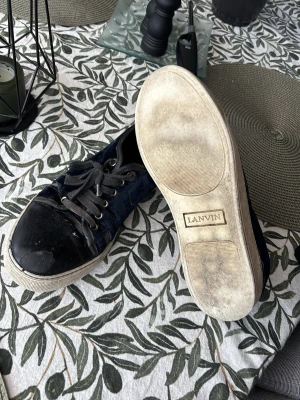 Svarta och blå sneakers från Lanvin - Snygga sneakers från Lanvin i svart och mörkblått med vita sulor. Ovandelen är i en mix av glansigt och matt tyg, med svarta skosnören och metallöljetter. Klassisk låg modell som passar till många olika stilar.