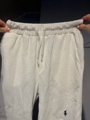 Vita mjukisbyxor från Polo Ralph Lauren - Säljer ett par vita mjukisbyxor från Polo Ralph Lauren med resår i midjan och dragsko. Byxorna har sidofickor och den klassiska Polo-loggan broderad på benet. Materialet är mjukt och strukturerat, perfekt för chill dagar.