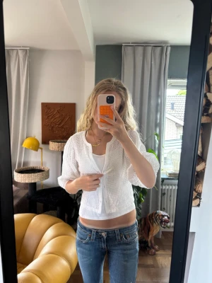 Vit blus med trekvartsärm - Söt vit blus med broderade detaljer och trekvartsärmar. Blusen är croppad och har en luftig passform, perfekt för varmare dagar. Stängs framtill med knappar och har en lätt struktur i tyget som ger en trendig look.