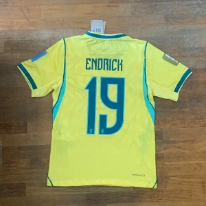 Brasilien VM tröja Endrick #19 - Snygg gul Brasilien fotbollströja från Nike med Endrick och nummer 19 på ryggen. Tröjan har blå och gröna detaljer, CBF-logga och Nike-logga på bröstet samt korta ärmar. Perfekt för dig som älskar fotboll och vill stötta landslaget.