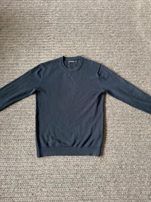 Mörkblå stickad tröja från Matinique - Passar M/L. En stilren mörkblå stickad tröja från Matinique med rund halsringning och ribbade muddar vid ärmslut och nederkant. Perfekt basplagg för lager på lager och enkel att matcha med olika outfits.