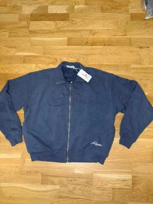 Blå ziptröja från Acne Studios - Snygg blå ziptröja från Acne Studios med broderad logga på bröstet och stor logga på ryggen. Storleken är S men den är så pass baggy att jag hade rekommenderat M