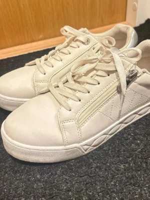 Vita sneakers med dragkedja - Stilrena vita sneakers i läderimitation med snörning och dragkedja på sidan.