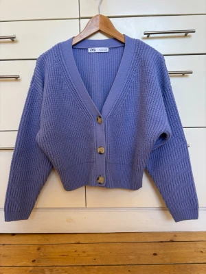 Blålila ribbad kofta från Zara, storlek S - Blålila kofta från Zara med ribbad struktur och v-ringning. Koftan har tre stora knappar framtill och är något croppad i modellen. Akryl, tjockt stickad. Lite noppig men fortfarande fin. Storlek S, passar även XS.