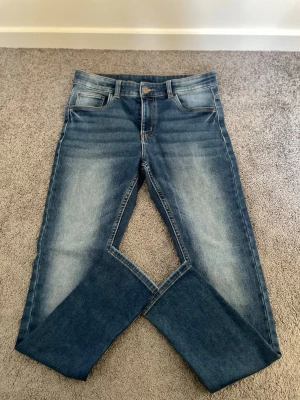 Blå jeans med tvättade detaljer - Säljer ett par klassiska blå jeans med snygga tvättade detaljer och raka ben. Jeansen har fem fickor, normal midja och är gjorda i denim. Perfekta till en avslappnad stil och passar till det mesta.