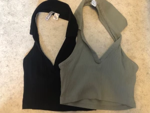 Två ribbade halterneck toppar - Säljer två snygga ribbade halterneck toppar i svart och ljusgrön färg. Båda har v-ringning och croppad passform, perfekta till sommaren. Materialet är mjukt och stretchigt, vilket gör dem bekväma och lätta att styla till olika outfits.