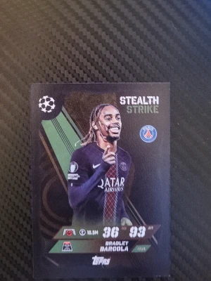 Match Attax PSG samlarkort Barcola - Samlarkort från Topps Match Attax Barcola med motiv av en PSG-spelare och texten 'Stealth Strike'. Kortet har svart bakgrund med gröna och vita detaljer samt PSG-logga. Perfekt för dig som gillar fotboll och att samla på kort.