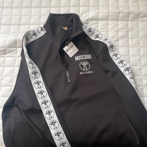 Moschino tröja - Moschino tröja köpt på wallenberg orginal priset står på andra bilden köpt på wallenberg i umeå den 5e  augusti 15:39 inga skador eller defekter strl L/52 swish ändast inget plick saftey eftersom de tar % av priset.(köpare står för frakt)dm för mer bilder