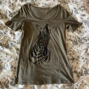 Militärgrön T-shirt med tryck av zebra och en vid urringning. Märke: Esprit. 3 för 2 på allt i min profil 🍓