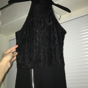 Festklänning.  - Klänning från Nelly. Aldrig använd.  Toppen är i spets och kjolen är i elastisk trikå med dekorativ dragkedja på framsidan. Väldigt snygg på. Midi-längd. 