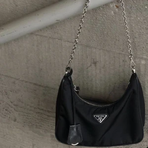Black Prada Re-edition 2005 Re-nylon bag - Tidlös Re-edition från Prada 🖤Kommer med kedja, axelband och en ”detacheble pouch” 🖤Sparsamt använd - skickar gärna fler bilder vid intresse 🖤Nypris: 19 000 kr 🖤Äkthetsbevis finns 🖤