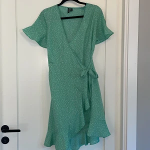 Omlottklänning  - Omlottklänning från Vero Moda. Använd få gånger. Sitter som den blåa klänningen på bilden. Klänningen är grönare i verkligheten💚