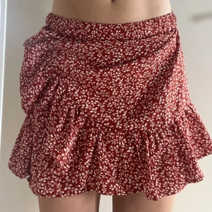 Röd och vitblommig kjol, volangkjol - En gullig röd volangkjol med vita blommor. Passar mig som har xs i storlek. Går att vika upp om man vill att den ska bli kortare. Köparen står för frakt:)