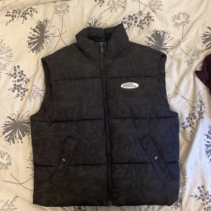 Väst  - En svart väst med mönster från hm som är unisex. Västen är i storlek S men som man ser på  bilden är den väldigt stor därför passar den även folk som har storlek M. Perfekt för hösten och vinter som man kan ha över en hoddie eller tjocktröj. Aldrig använd