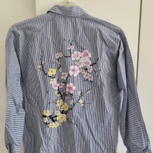 Blå randig skjorta - Blå/vit randig skjorta med broderade blommor på baksidan. Från Zara, storlek S. Knappt använd