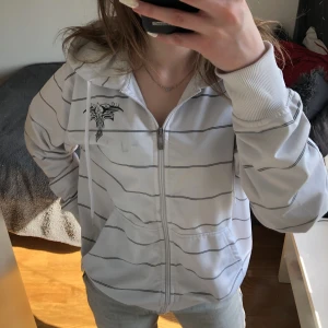 Zip-up hoodie - Säljer den här snygga, vita zip-up hoodien med svarta ränder och tryck. Bra skick. Säljer då jag inte använder den längre 😋