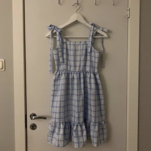 Blå klänning - Ljusblå och vit rutig klänning med knyten i axlarna. Klänningen är i storlek xs