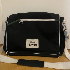 Lacoste väska - Vintage lacoste väska som inte går att få tag på längre, retro sport 20 modell. Fint skick men finns tecken på användning, banden är till viss del smutsiga men ingenting man tänker på<3 Stor nog att ha dator och mycket annat i!  OBS!! frakten är 120kr!