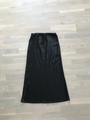 Svart satinkjol strl 36 - Svart satinkjol från Mango i storlek 36, inga anmärkningar i skicket. Har resårband högst i midjan och är vadlång, hör av er vid frågor!