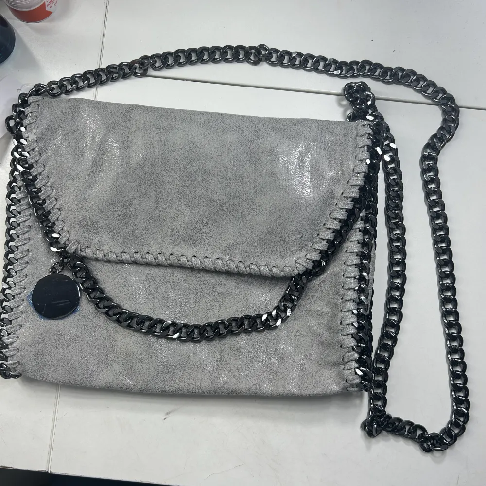 En linande Stella McCartney väska i färgen ljusgrå, den är ljusare i verkligheten. Helt ny och när med aldrig använd. Prislapp och skydd för den runda metallbrickan är kvar. Det är den lilla modellen men den är väldigt rymlig ändå💗Skriv vid intresse🔥🔥. Väskor.
