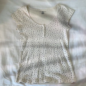 Blommig t-shirt - Vit t-shirt från brandy Melville med blåa små blommor på och lace i nacken💞🤘🏼 Den har knappar som går att knäppa upp. Perfekt skick👍🏼Fråga om frakt. 
