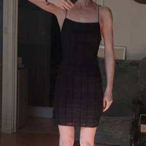 Rutig klänning - Fodralklänning i minilängd. Rutigt svart tyg. Axelbanden korsade i ryggen.  Ny med lapp kvar!