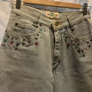 Högmidjade jeans med färgglada stenar på fickorna. Lite 80-tals stil på dom då dom ser lite ut som mom jeans. Använd kanske 3 gånger för 3 år sen.