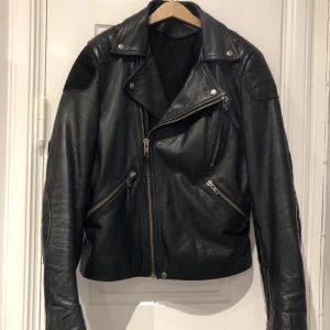 Acne skinnjacka  - Tidlös skinnjacka med mockadetaljer från Acne i storlek 48 herr. Sparsamt använd och i mkt gott skick. Modell Theo AW/10 (Pop Classics). Se bilder för detaljer och hör av dig vid frågor. Skuldermått: 40 cm. Armlängd: 87 cm (inkl. Axel). Rygg: 65 cm. 