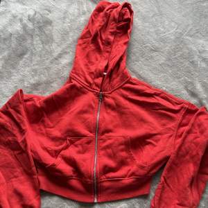 En röd zip-hood från H&m som även är en kortare variant. Inte använd någon gång då köpet blev i fel storlek!