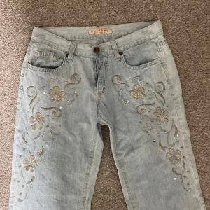 Lågmidjade jeans med brodyr  - Jeans med låg midja med brodyr på framsida lår köpta i Spanien. Straight leg / ganska breda och långa. 