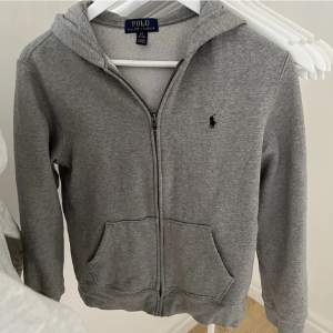 Det är en grå polo zip hoodie. Den är knappast använd mest legat i garderoben. Nypris 1095. Storlek 14/16 år.