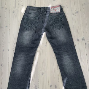 Gråa True Religion Jeans - Sjukt snygga ovanliga gråa True Religion jeans!!! med snygg tvätt och straight fit men klippta ner till för en mer bootcut passform. Midjemått tvärs över: 40cm, Innerbenslängd: 78cm. Skriv för mer frågor eller bilder!😊Priset är inte hugget i sten!