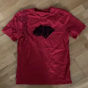 En enkel oanvänd röd t-shirt med ”björnarna” loggan från Wildkids! En superenkel utklädnad till halloween, du behöver bara lägga till lite svarta streck på kinderna 😍   OBS det är lite svart sprayfärg i hörnet på ena ärmen från när jag sprayade den :)