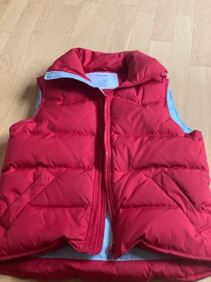 Dunväst Boomerang - Fin röd dunväst med ljusblått foder. Storlek Small