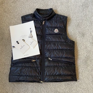 Moncler Navy Gui Vest - Äkta Moncler gui väst som är köpt på Mytheresa i storlek 3/L. Haft den ett tag men inte mycket använd och har tvättat den (enligt monclers guidelines), skulle därför säga att skicket är 9,5/10. Kvitto, lappar mm med följer. Ny pris 8500! Skriv för Bilder.