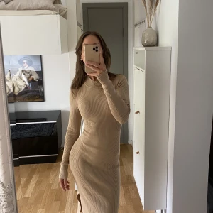 Ribbstickad klänning  - Beige klänning i nyskick (aldrig använd då jag inte tycker färgen passar på mig). Slits på sidan och vadlång på mig som är 169 cm. Fin passform och bekvämt material