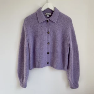 Stickad tröja med knappar  - Mjuk och skön stickad tröja med knappar och krage i ljus lila färg. Skick: använt  Material: 40% alpacka 25% ull 35% polyamid  Nypris: ca 700kr  