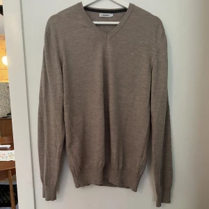 J. Lindeberg ulltröja - Grå/beige J. Lindeberg tröja i merinoull i mycket fint skick. Den har ett väldigt litet hål längst ned på den vänstra ärmen (se bild 3), men det är knappt märkbart. Skriv för fler bilder⭐️